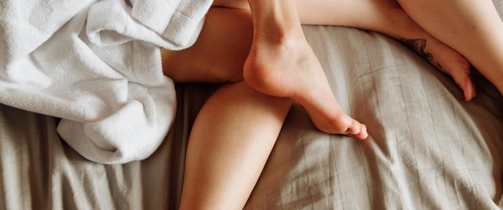 A warm and cozy scene of intertwined legs on a bed with white robes, conveying intimacy and comfort.