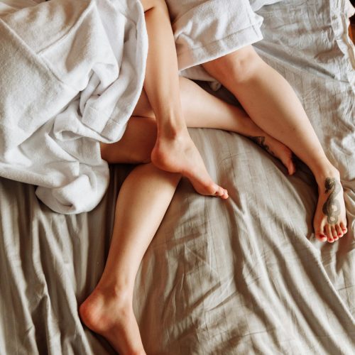 A warm and cozy scene of intertwined legs on a bed with white robes, conveying intimacy and comfort.